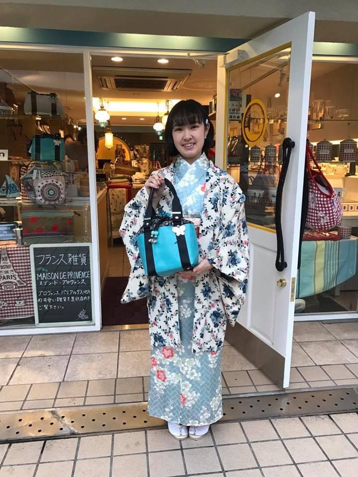 Jeune femme en kimono tenant un sac turquoise devant la boutique Maison de Provence